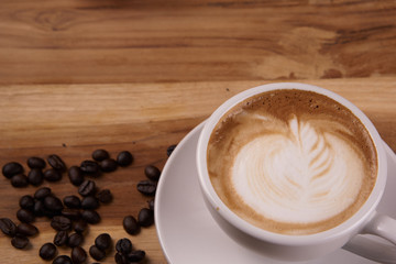 Cappuccino or latte art coffee. Free hand pouring some foam of milk on top. A white ceramic cup on the wood table with some coffee beans. The best food and drink in the world. Fresh energy everyday.
