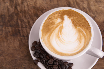 Cappuccino or latte art coffee. Free hand pouring some foam of milk on top. A white ceramic cup on the wood table with some coffee beans. The best food and drink in the world. Fresh energy everyday.
