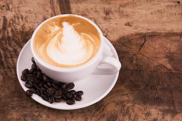 Cappuccino or latte art coffee. Free hand pouring some foam of milk on top. A white ceramic cup on the wood table with some coffee beans. The best food and drink in the world. Fresh energy everyday.