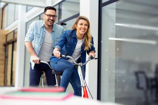 Two Happy Coworkers Riding Bicycle In The Office Together. Making People Laugh.