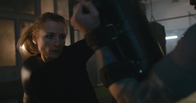 Female boxer practicing hits with her coach in a boxing studio at night. 4K UHD
