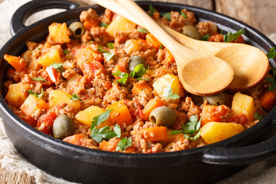 picadillo is a traditional dish made with ground beef, potatoes, onions, garlic, cumin, carrots, white wine, tomato sauce, raisins, olives and capers closeup. horizontal