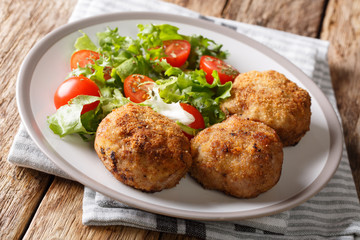 Tasty Danish pork minced meat patties in breading with fresh vegetable salad close-up on the table. horizontal