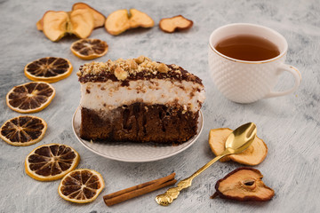 Festive dessert. A piece of chocolate cake with nuts. Cinnamon stick, dried lemon wedges, pears, Apple. White mug with tea. Light background.