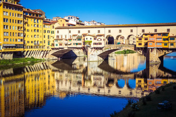 Panoramic view of the Arno River and stone medieval bridge Ponte Vecchio with beautiful reflection of colorful houses, Florence, Tuscany, Italy.