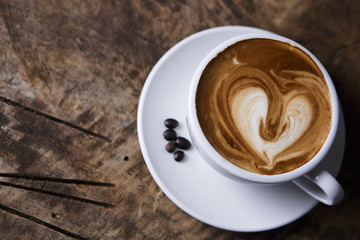 Hot cappuccino or latte art coffee. A cup of coffee on the wooden table with roasted beans. Morning breakfast with coffee. Hearts shape created by pouring steamed milk.