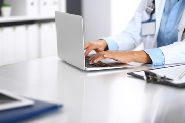Unknown doctor woman typing on laptop computer while sitting at the desk in hospital office. close-up of hands. Physician at work. Medicine and health care concept