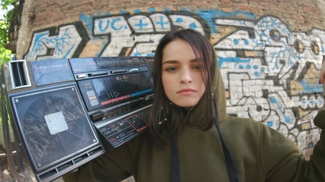 Awesome happy girl with straight black hair holding portable stereo boombox. Daytime. Hip-hop culture. Conceptual street. Lifestyle. Outdoors. Enjoy.