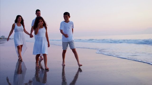Young Spanish family walking together on the beach at sunset