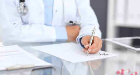 Doctor woman filling up prescription form while sitting at the desk in hospital close-up.  Physician at work and ready to give an advice to help patient. Healthcare, insurance and excellent service i