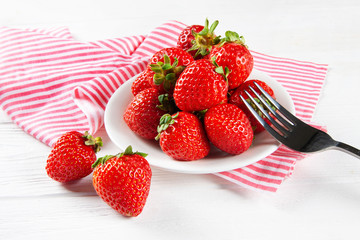 Fresh ripe strawberries on a plate. White wooden table, napkin in red and white stripes.