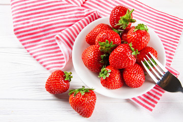 Fresh ripe strawberries on a plate. White wooden table, napkin in red and white stripes.