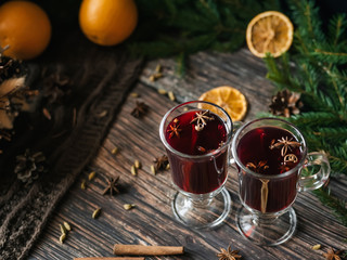 two glasses of mulled wine with spices and orange slices on a wooden table. Hot alcoholic drink on the background of Christmas decor with fir branches and cones