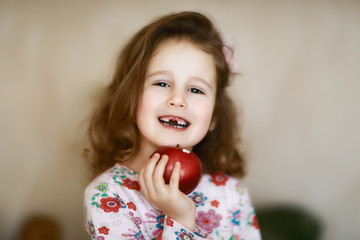 portrait of a happy child who has lost milk teeth, cute little curly toothless caroque girl smiles and holds in her hand a red apple