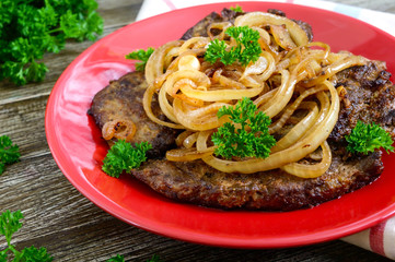 Juicy slices of fried liver and onions on a red plate.