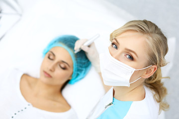 Naklejka premium Professional beautician doing eyebrow tattoo at woman face. Permanent brow makeup in beauty salon, closeup. Cosmetology treatment
