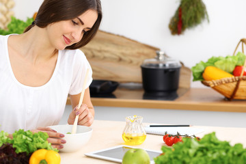 Beautiful Hispanic woman cooking in kitchen while using tablet computer and wooden spoon. Housewife found new recipe for dinner or breakfast. Healthy meal and householding concepts