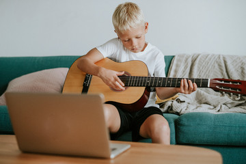 Boy learning to play guitar through a video call with his teacher