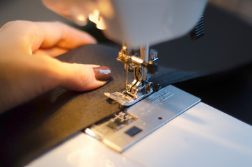 Fototapeta na wymiar master sews fabric product with a sewing machine on a dark background