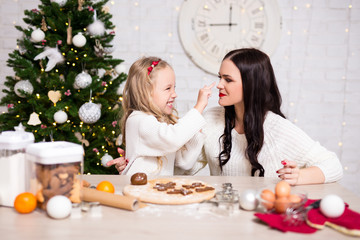 Obraz na płótnie Canvas Happy woman and her daughter cooking Christmas cookies in kitchen with Christmas tree