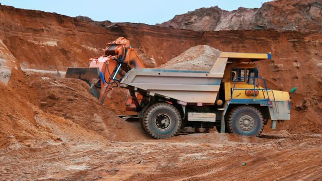 Excavator loading sand into dumper truck. Crawler excavator working