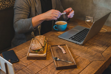 Fototapeta na wymiar man hands working on laptop in cafe eating sandwich drinking coffee