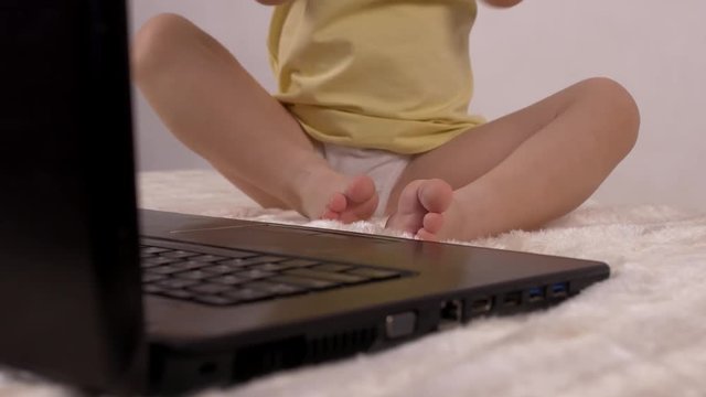 A small child presses a finger on the button on the laptop keyboard, close-up, baby and computer, relaxation