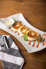 Cottage cheese pancakes with sour cream on white plate on wooden background