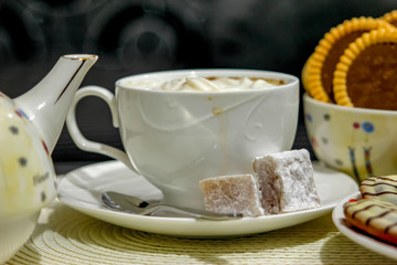 Coffee with cream and cakes on table. Big mug of coffee, sweet cakes and old ewer in modern surrounding of living room.