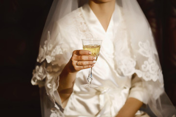 Bride with a glass of wine in a white peignoir with a ring on her hand, bride's morning
