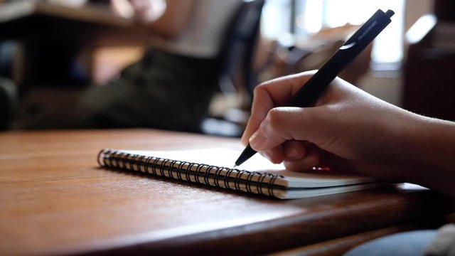 Slow motion of a woman's hand writing on blank notebooks on wooden table 