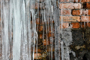 large icicles abstract old brick wall background with crack ice, moss, and branches of bushes, set