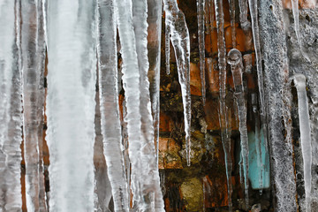 closeup icicles, abstract old brick wall background with crack ice, moss, and branches of bushes, icicles, ice build-up on brick wall