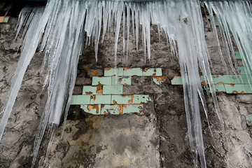 icicles hanging from the roof of the old brick building with cubes of old tiles, traumatic acrid ice, thaw in the early spring, set