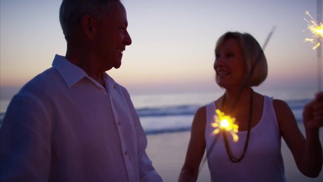 Senior Caucasian couple dancing with sparklers on ocean beach at sunset