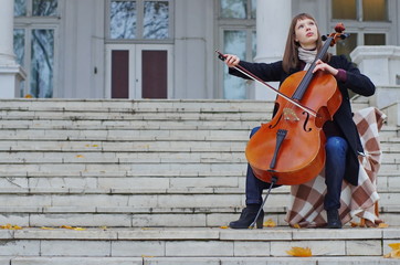 young woman playing cello on the steps of marble staircase of an ancient house © Julia