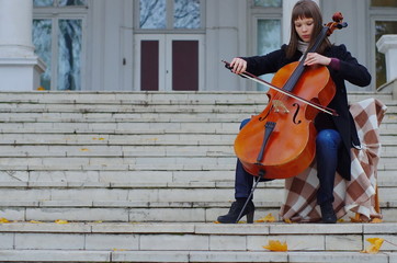 young woman playing cello on the steps of marble staircase of an ancient house © Julia