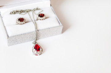 Jewelry set with red gems in the box close-up. Silver necklace and earrings with ruby gem. Gift,...