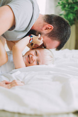 Fototapeta na wymiar father kissing his litle son on the bed with white linen