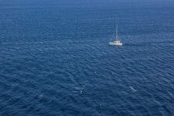 Obraz premium summer holidays concept of sea waves surface and small white yacht from above aerial shot, copy space 