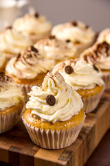 Tiramisu cupcakes decorated with cocoa powder and coffee grains on a wooden board next to jugs of milk, cream and a cup of coffee
