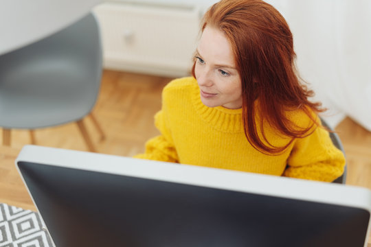 Young redhead woman working at a desktop monitor