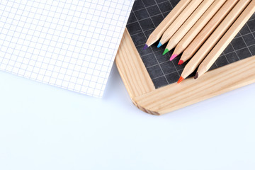 colored pencils, blackboard and a paper bloc paper sheet  isolated on white background