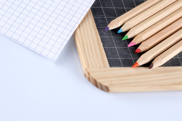 colored pencils, blackboard and a paper bloc paper sheet  isolated on white background