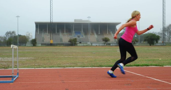 Female athlete jumping over hurdles on a running track 4k