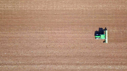 Fototapeta na wymiar Green Tractor cultivating and seeding a dry field - Top down aerial image
