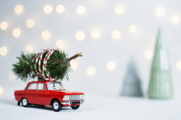 Red toy car with a christmas tree on the roof and garland lights bokeh on the background