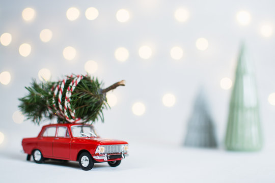 Red Toy Car With A Christmas Tree On The Roof And Garland Lights Bokeh On The Background