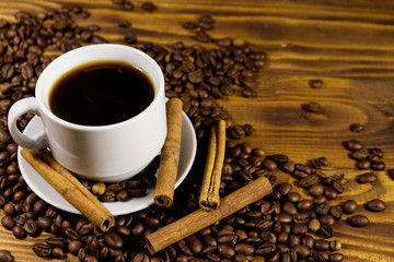 Cup of coffee, roasted coffee beans and cinnamon sticks on wooden table