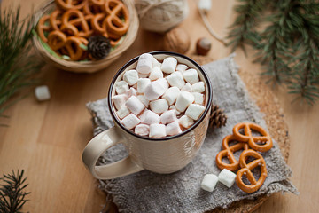 A cup of hot latte with marshmallows and some salty pretzels on wooden table. Christmas time, winter season.
